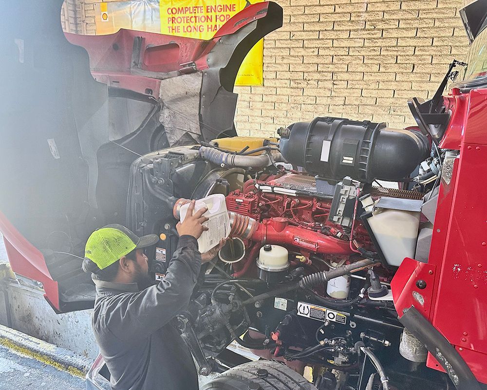A man is working on the engine of a red truck.