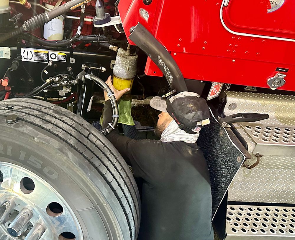 A man is working on the underside of a red semi truck