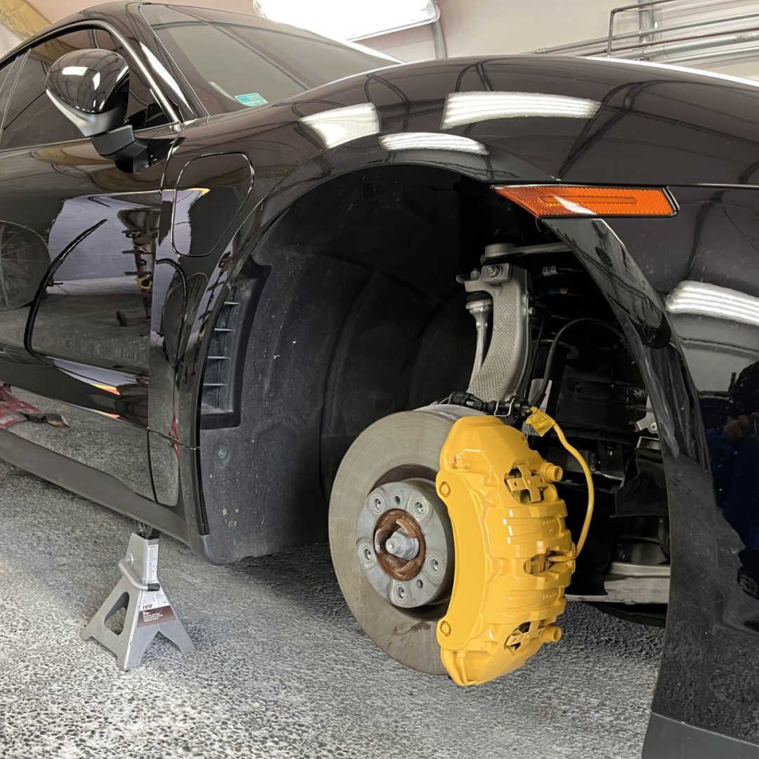 A black car with a yellow brake caliper on the front wheel