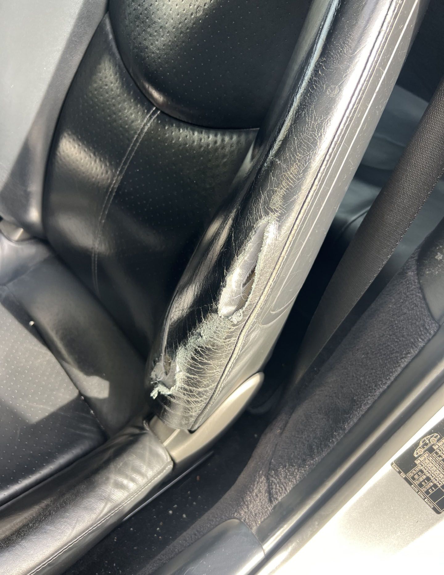 A black leather car seat with a tear in it