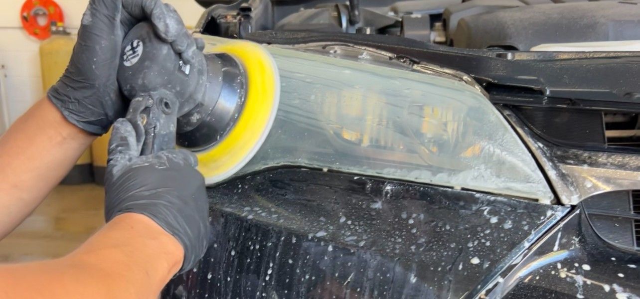 A person is polishing a car headlight with a sander.