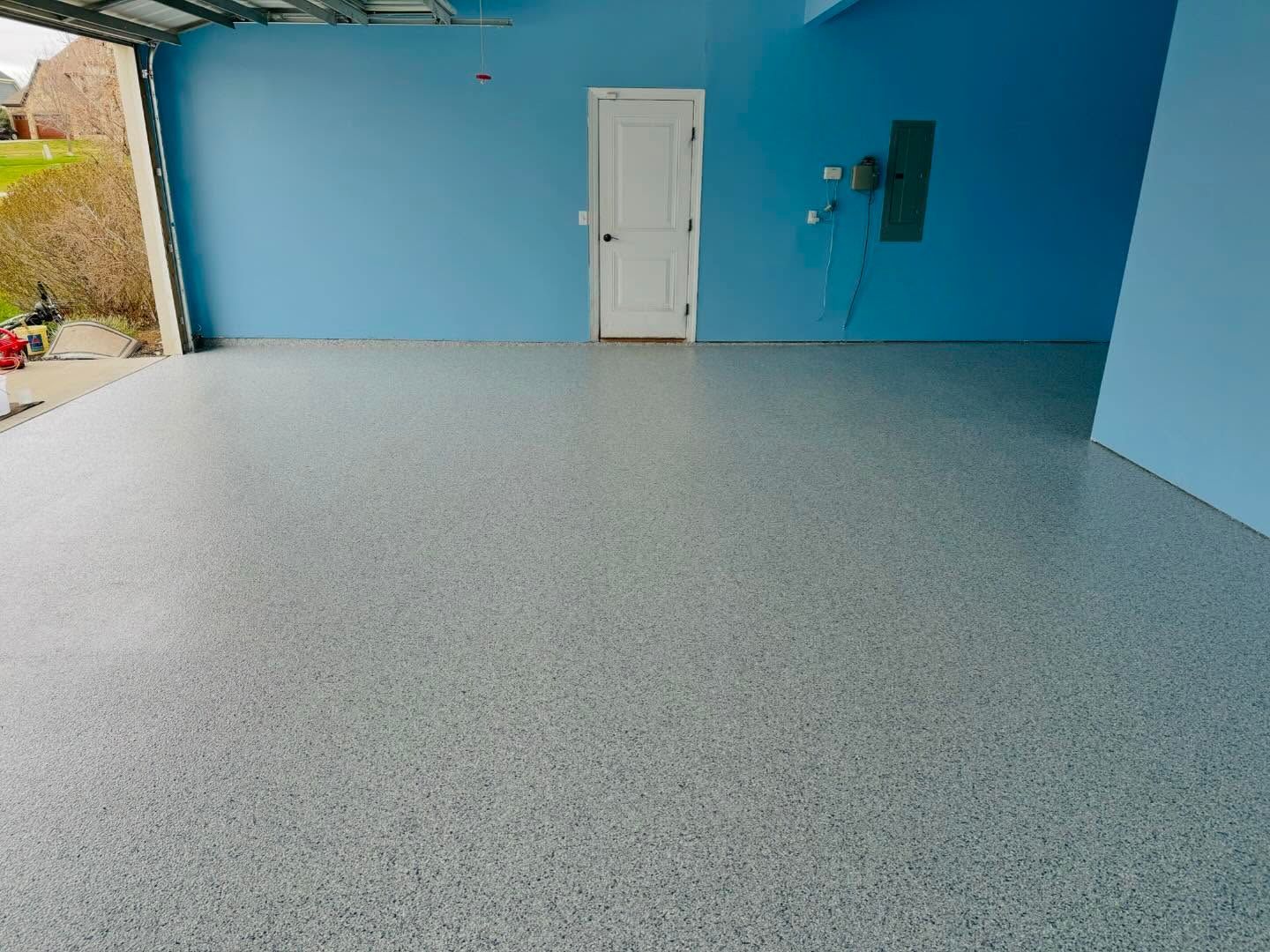 Garage interior with blue walls and a speckled gray epoxy floor. A white door is visible.
