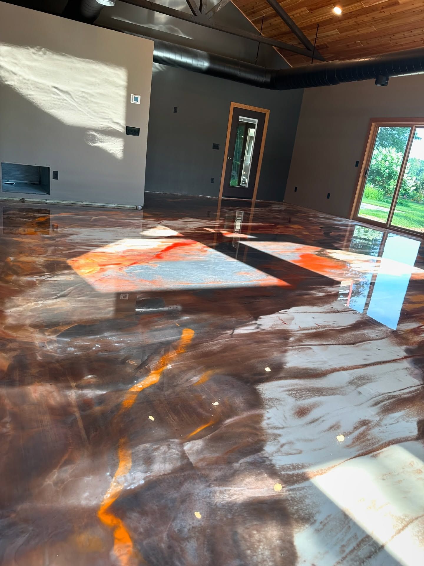 Metallic epoxy floor with red and gold hues in a large room, natural light, fireplace and doorway.
