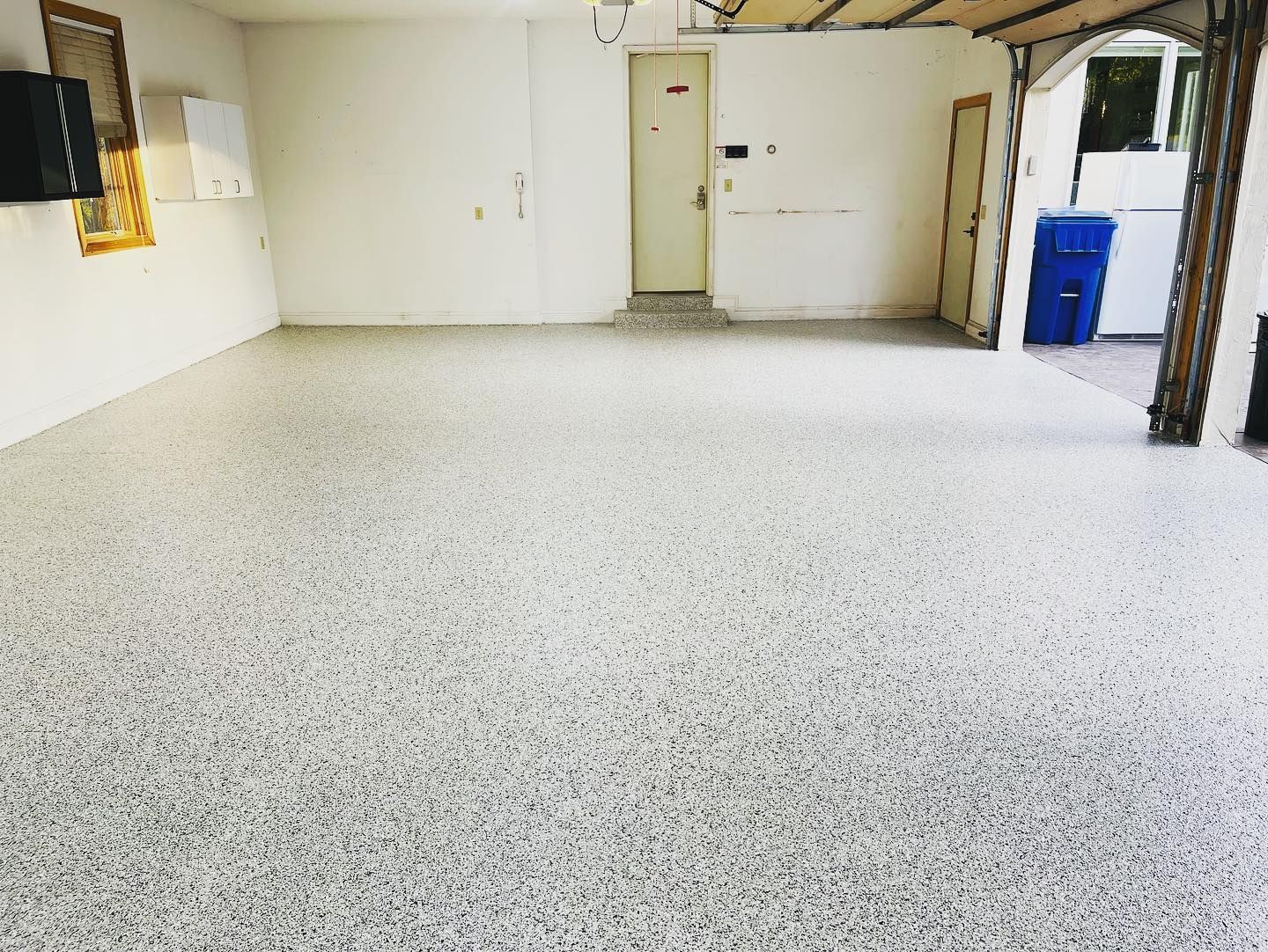 Garage with speckled gray epoxy flooring, white walls, and a closed door.