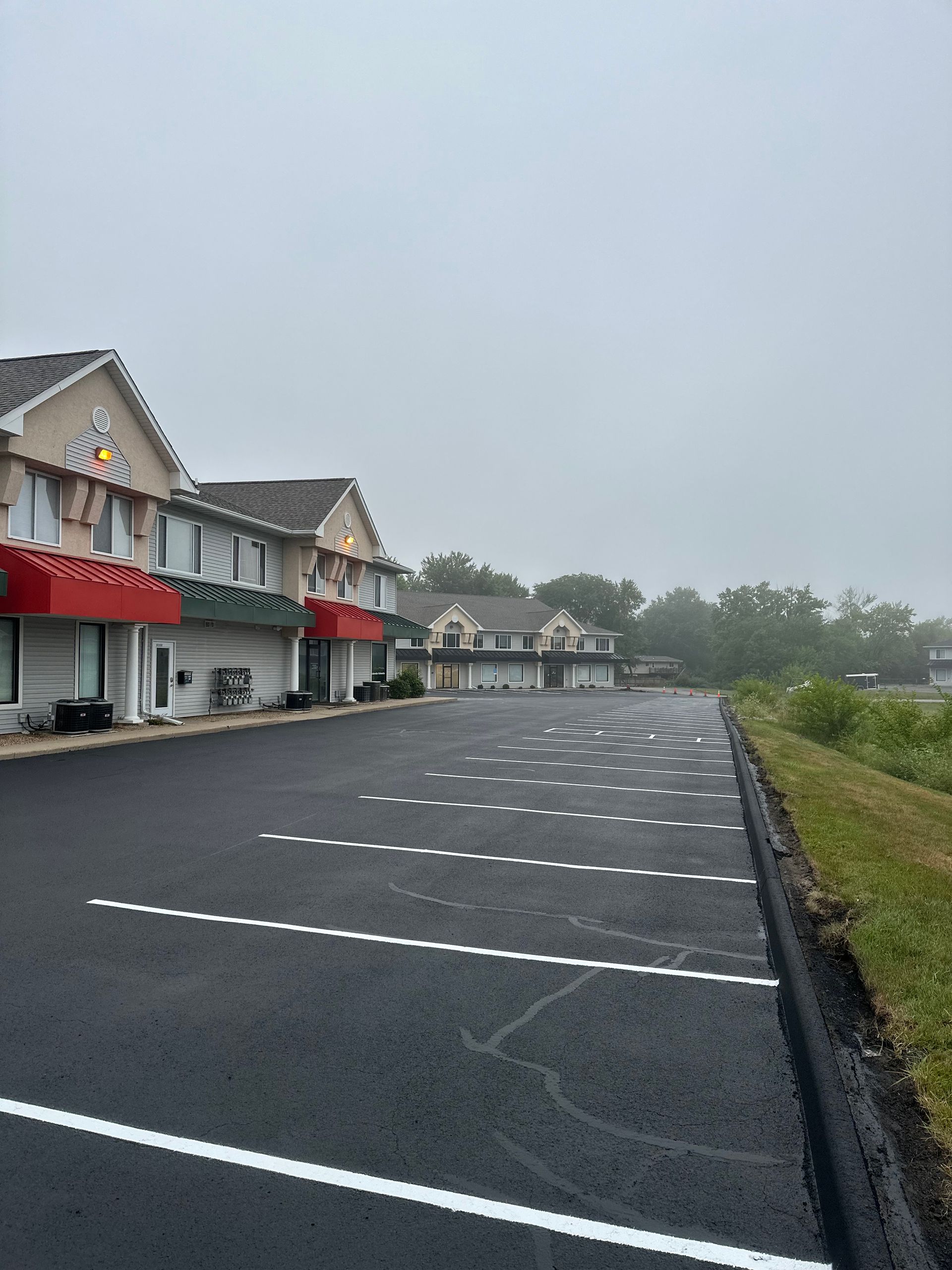 Motel exterior with freshly paved parking lot on a cloudy day. Red awnings and landscaping present.