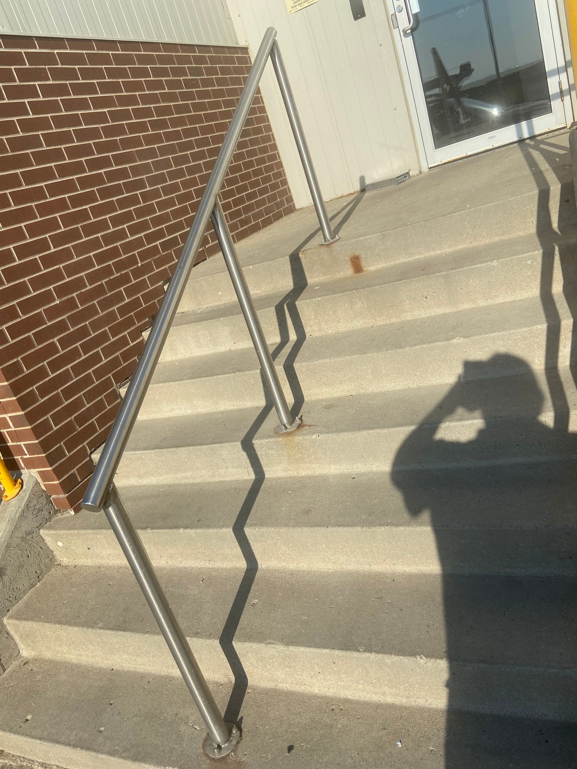 Concrete stairs with metal handrail. Brick wall to the left, door on the right. Shadow of a person on the stairs.