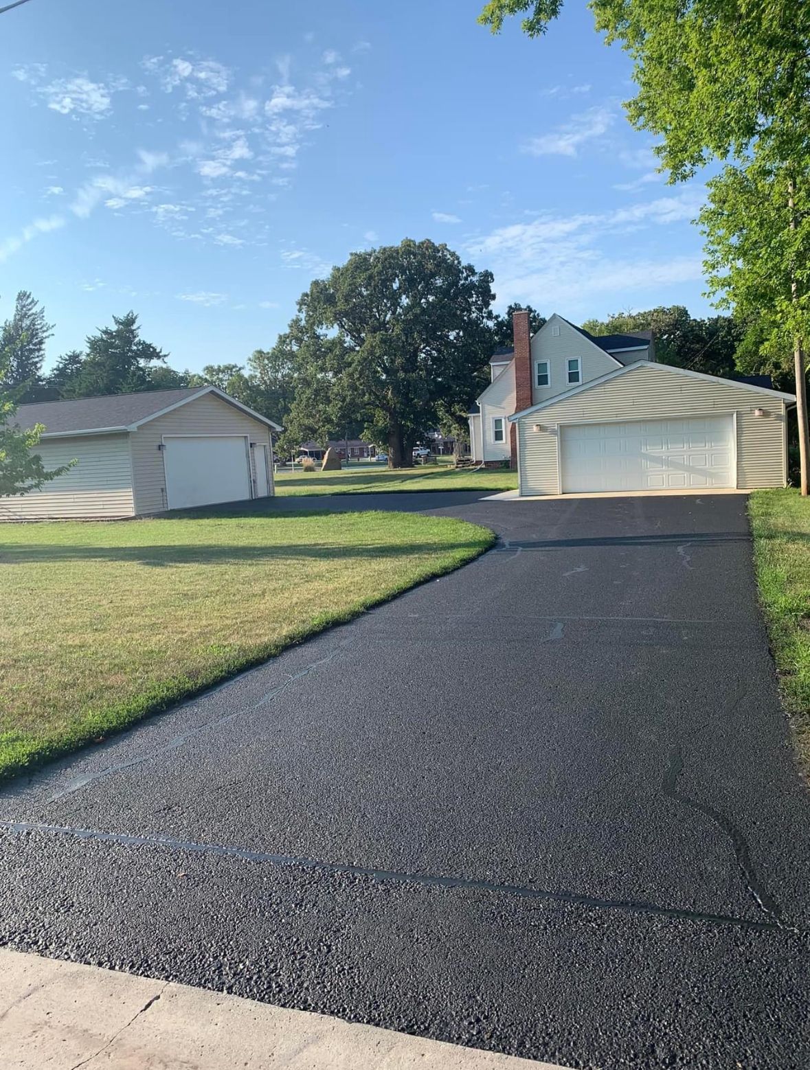 Newly paved asphalt driveway leading to a two-car garage. Houses and trees in background.