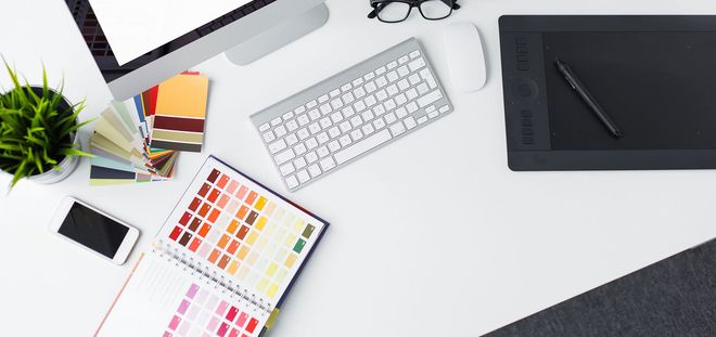 Desk with keyboard, pen tablet, color swatches, notebook, phone, and plant on a white workspace