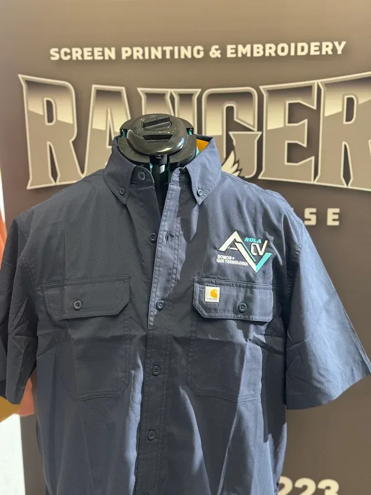 Blue short-sleeve work shirt on a mannequin in front of a “Screen Printing & Embroidery” sign