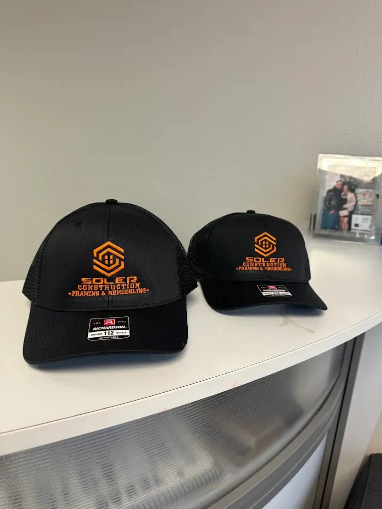 Two black baseball caps with orange logos on a white shelf, next to a small framed photo.