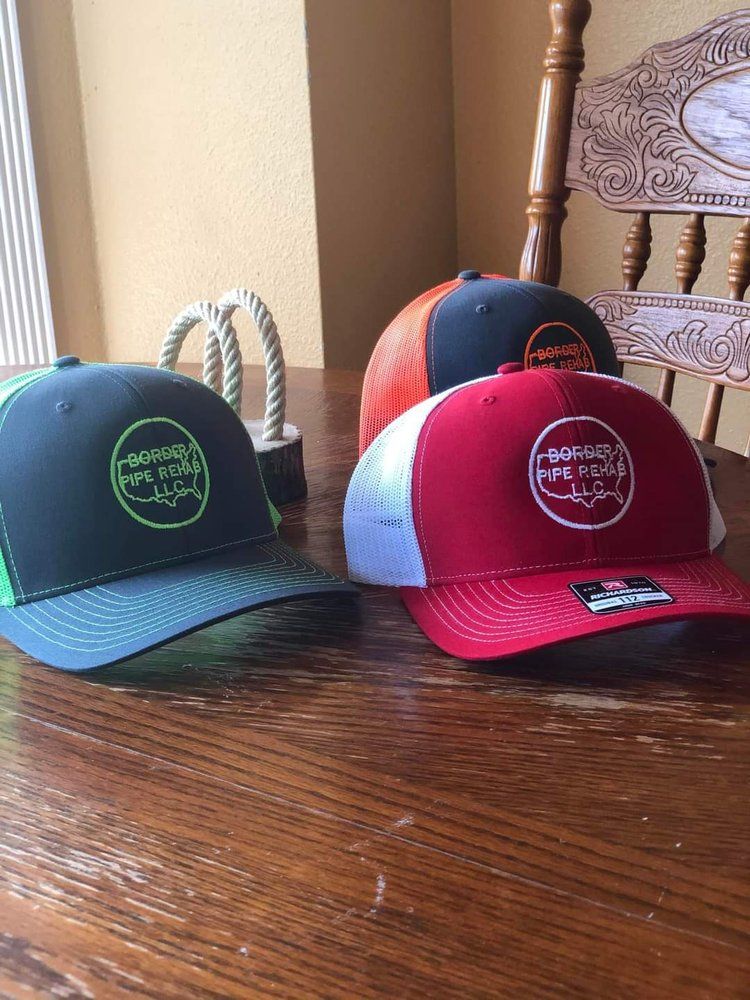 Four baseball caps on a wooden table: navy, black, orange, and red with white mesh backs.