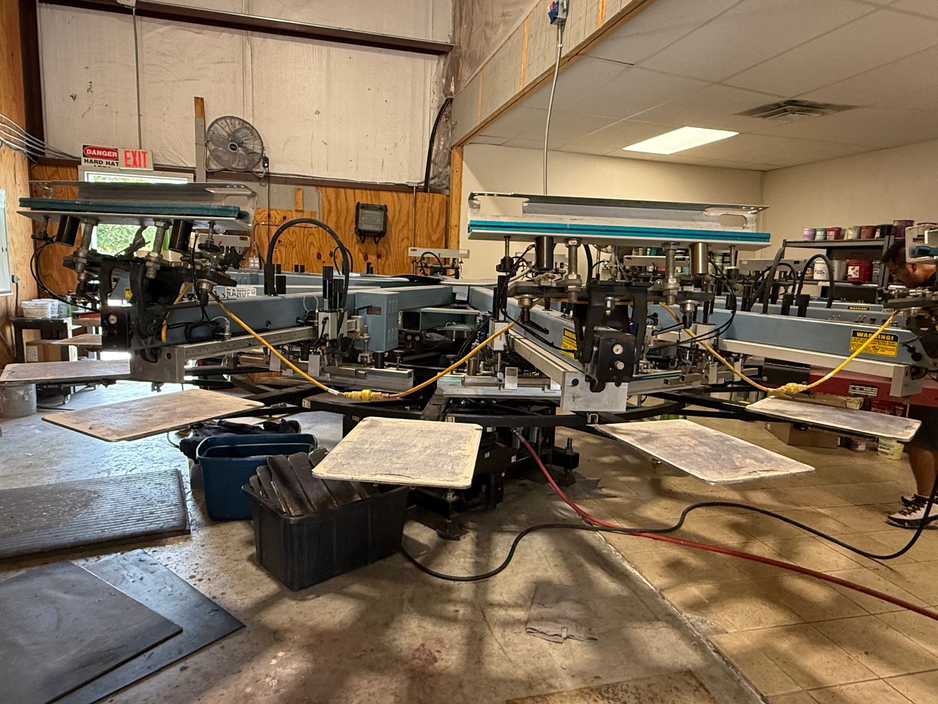 Screen printing workshop with multiple presses, tables, and equipment in a cluttered industrial space