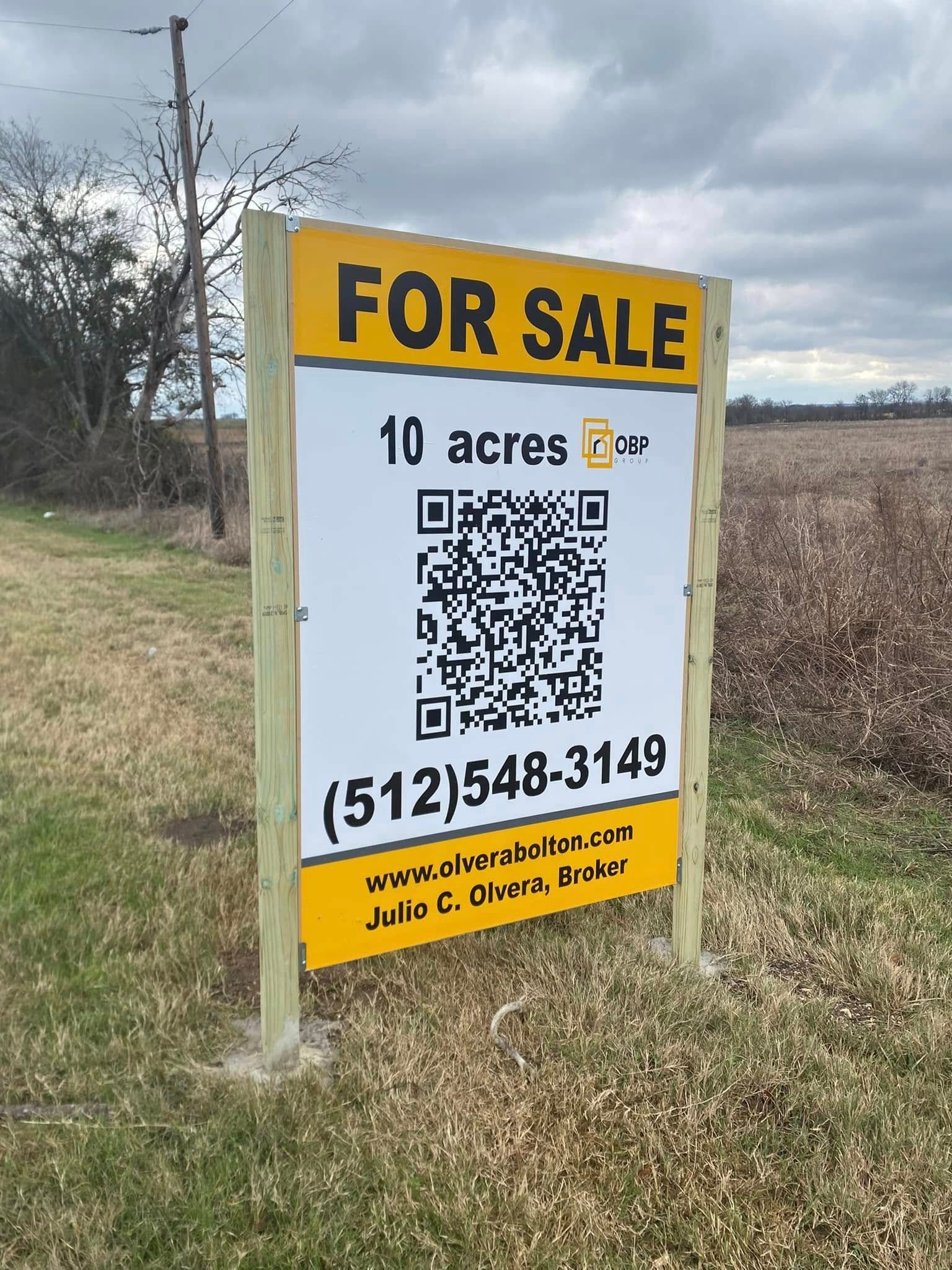 For sale sign on a grassy lot advertising 10 acres with a QR code and phone number.