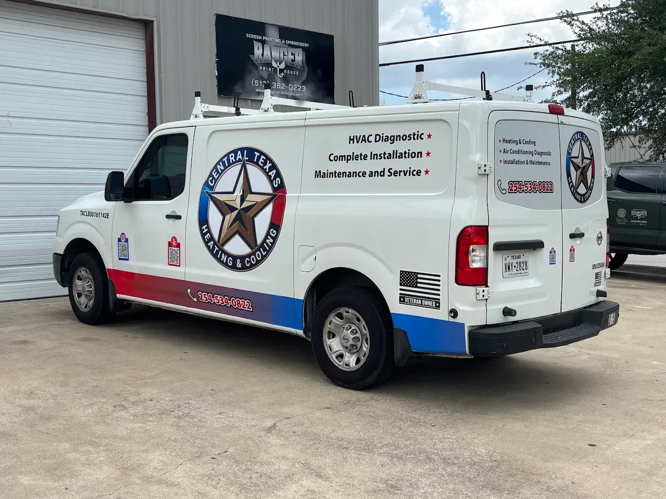 White service van with a star logo parked outside a garage, viewed from the rear side.