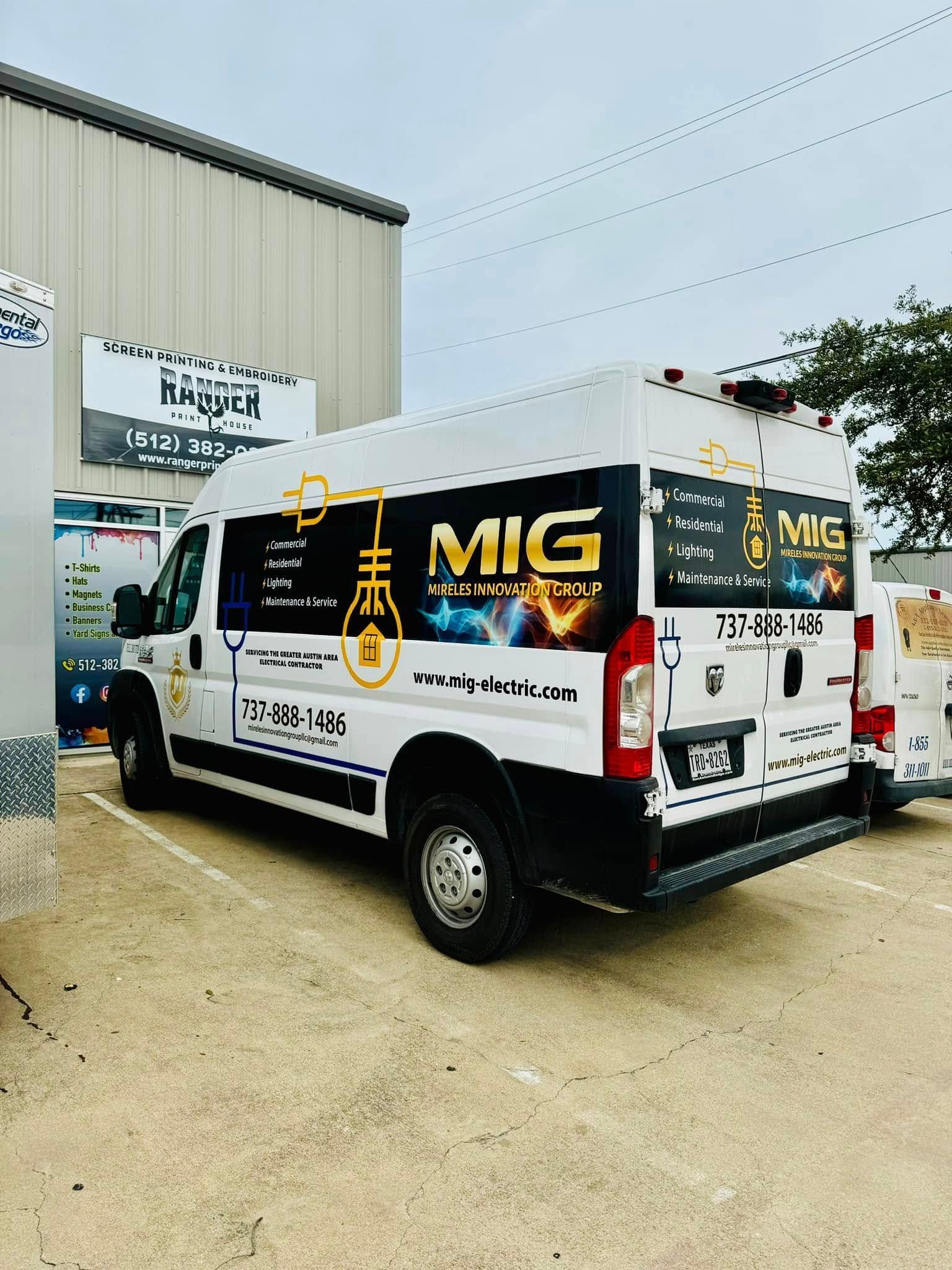 White MIG-branded cargo van parked outside an industrial building with equipment signage and trees nearby