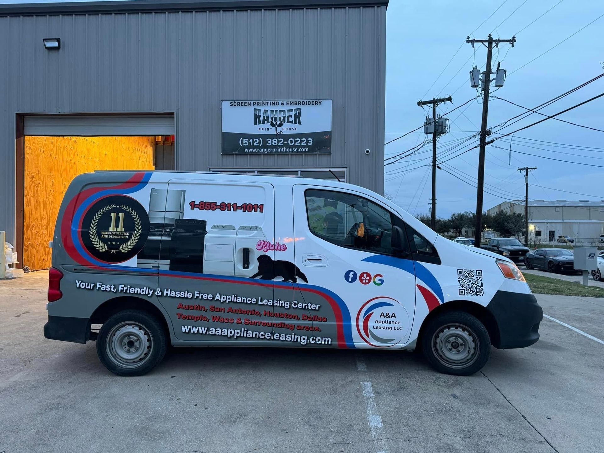 Wrapped white service van with red and blue graphics parked outside a gray industrial building at dusk.
