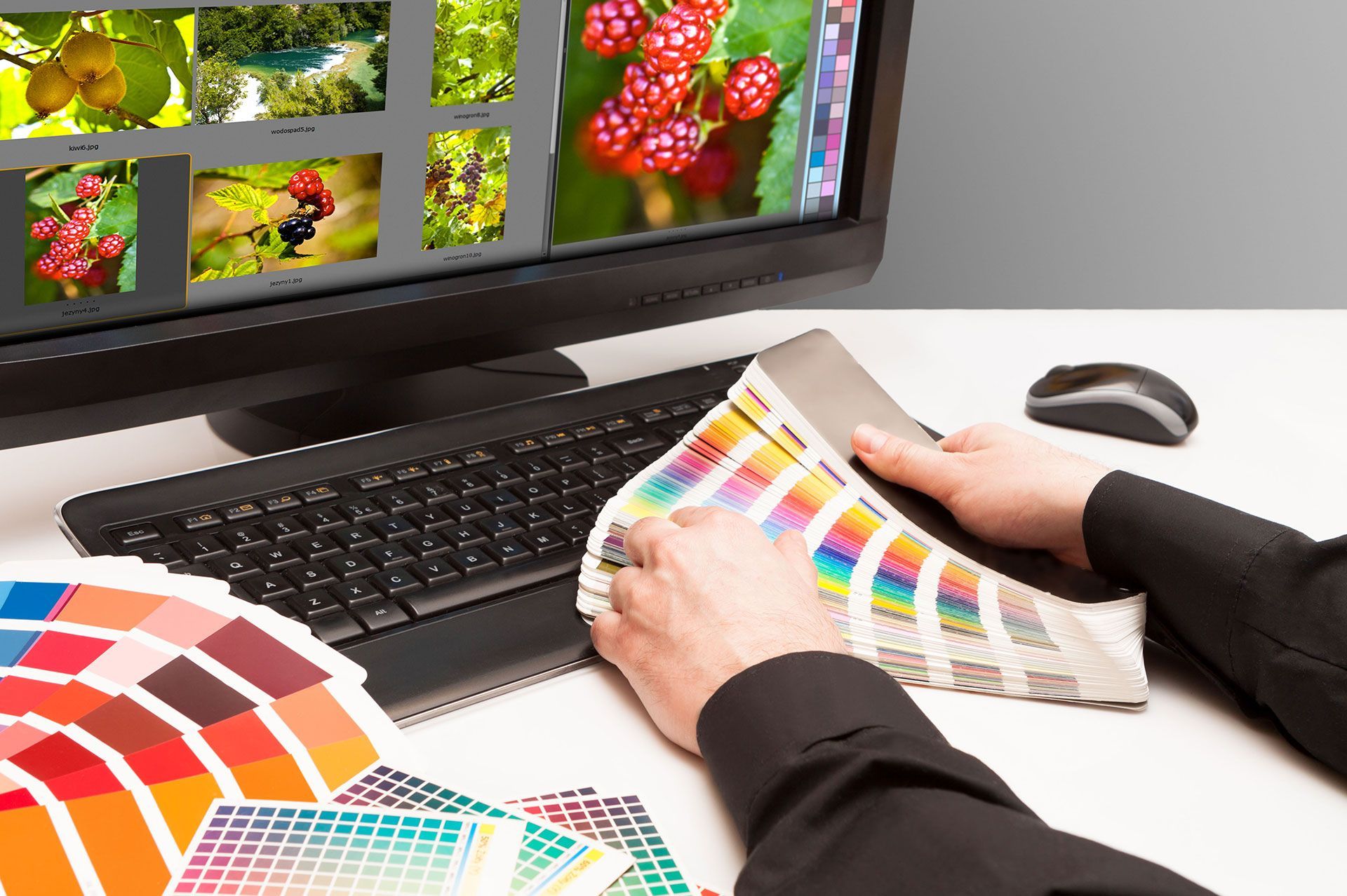 Hands reviewing color swatches beside a monitor showing a design layout