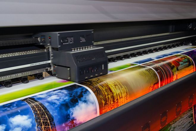 Large-format printer producing a colorful glossy banner with vibrant blue, orange, and red graphics