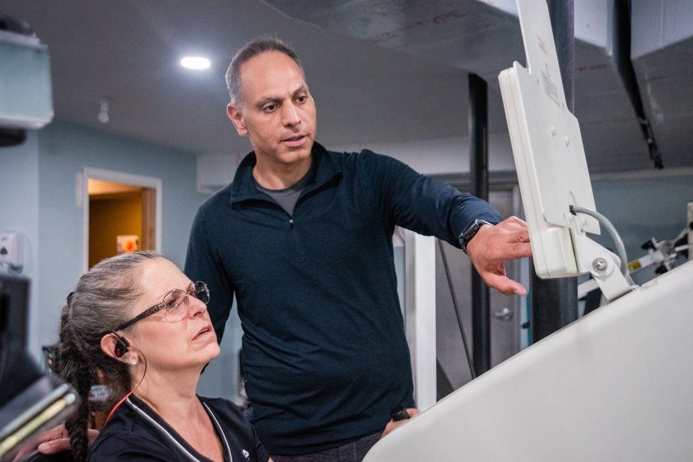 A professional instructor points to a screen while guiding an operator at a clinical workstation.