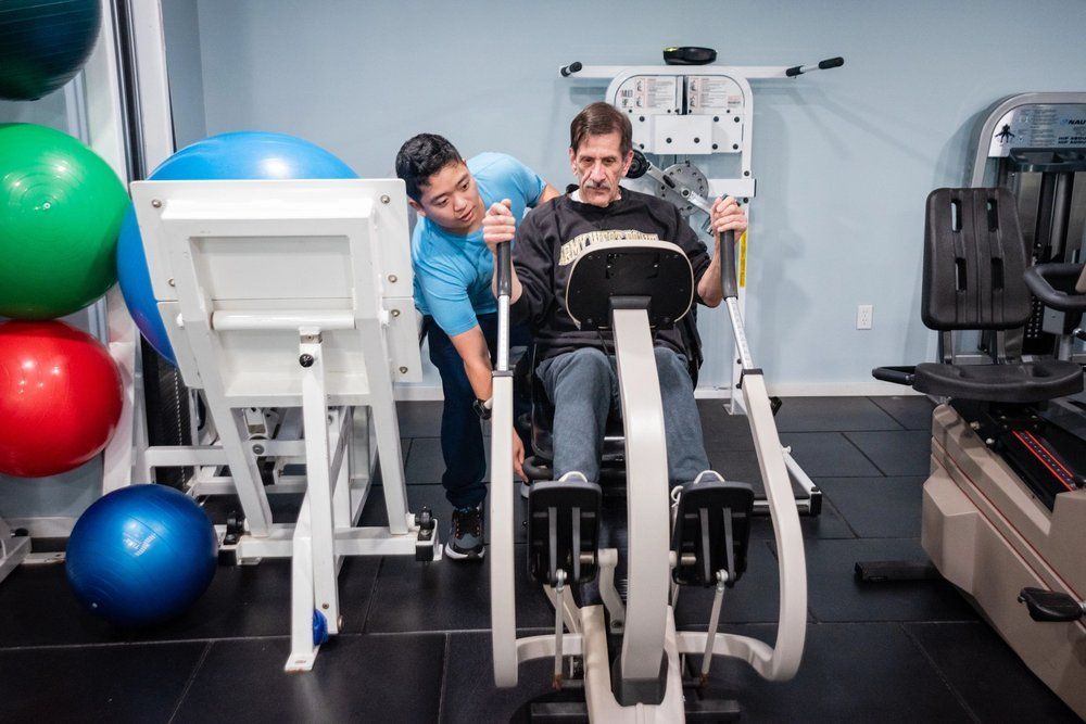A therapist guides a patient using an adaptive exercise machine in a physical therapy clinic.