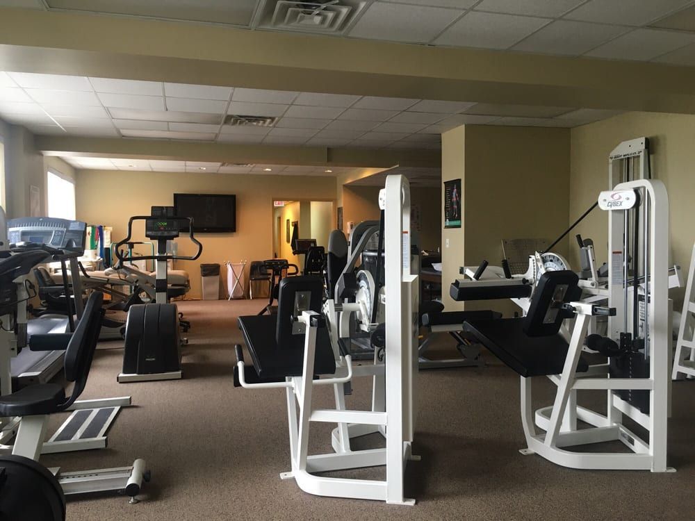 A gym featuring several pieces of weight training and cardio equipment set on a tan carpeted floor.