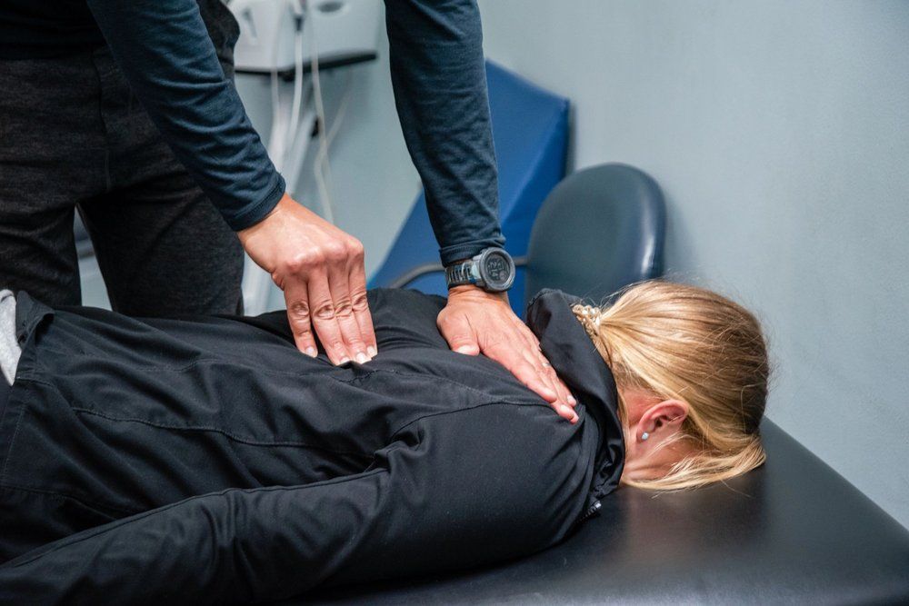 A practitioner performs a manual therapy adjustment on the upper back of a person lying on a treatment table.