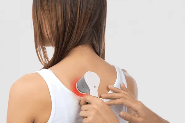 A hand uses a handheld device with a red light to treat a person’s upper back.