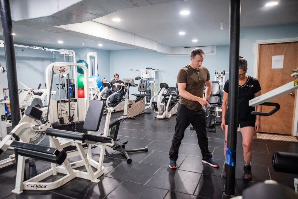 A physical therapist guides a person using a resistance band at a gym with exercise equipment.