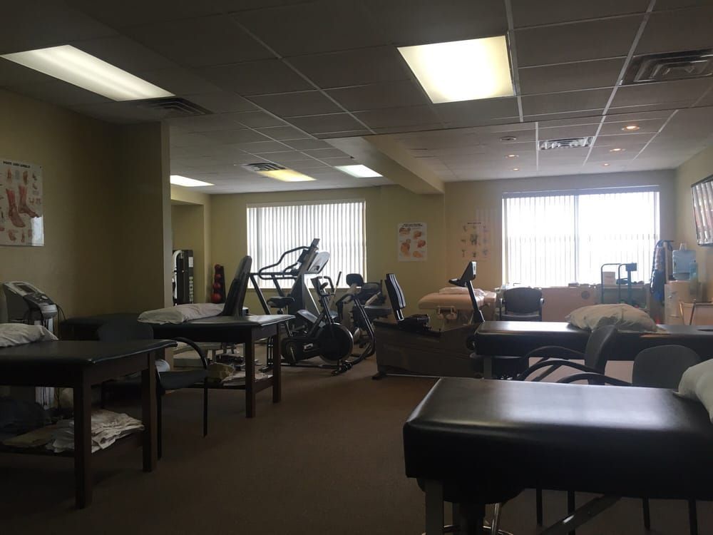 A physical therapy clinic with several examination tables and exercise equipment like stationary bikes.