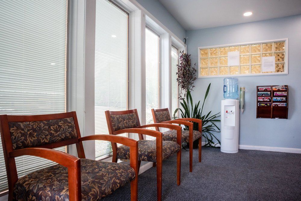 Three waiting room chairs arranged by tall windows next to a water cooler and a wall-mounted brochure rack.