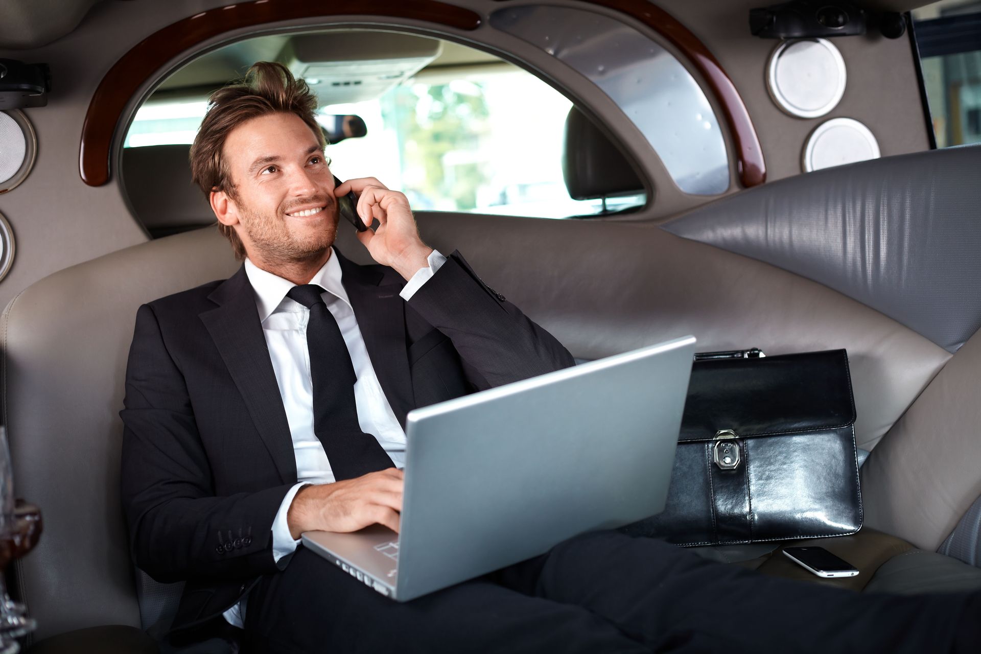 A man in a stylish suit sits comfortably inside Rockford Rides limousine, holding a laptop.