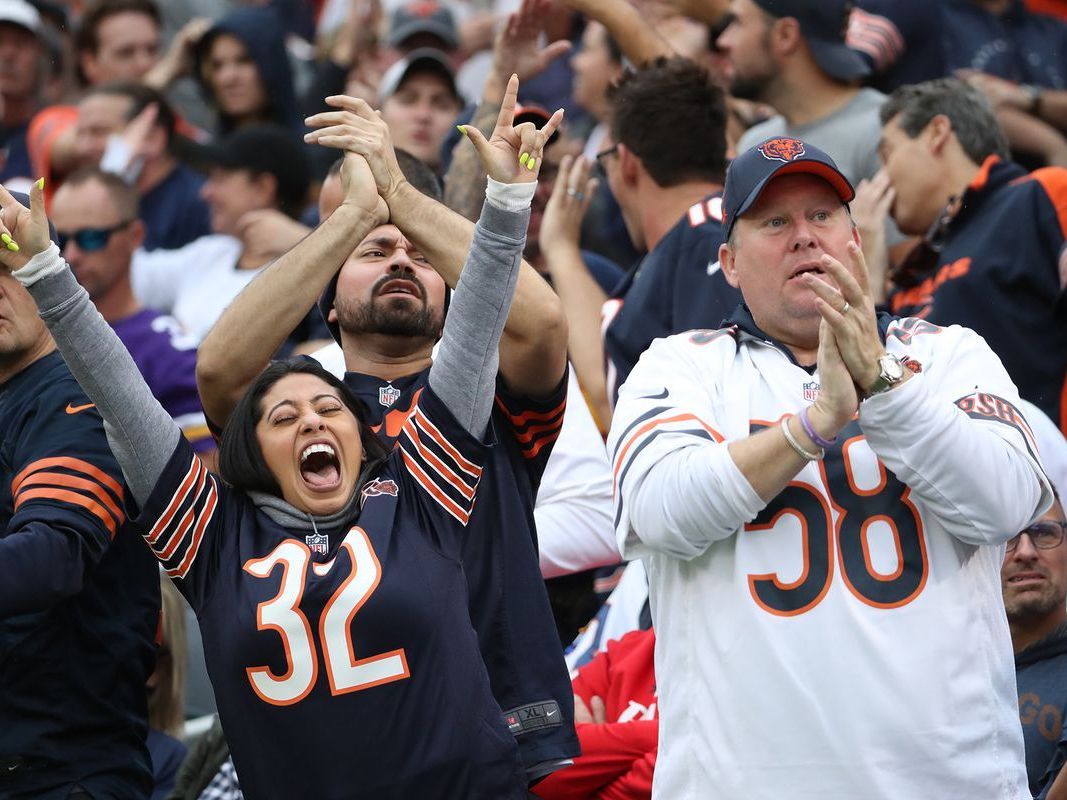 Two exuberant Chicago Bears fans are enjoying the game day atmosphere, dressed in team jerseys and sporting playful accessories like sunglasses, a headband, and fake mustaches. They embody the high spirits and camaraderie that fans can expect when traveling to a Bears game with Rockford Rides, which offers party bus services from Rockford to Chicago, ensuring fans arrive at Soldier Field ready to cheer on their team.