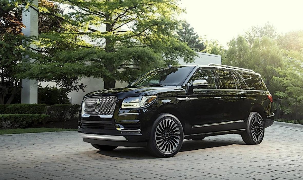 A luxurious black SUV limousine parked on a cobblestone driveway in front of an upscale home
