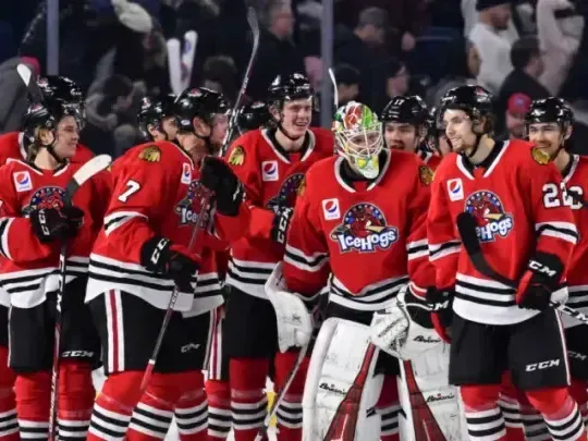 A smiling family of four is taking a selfie at an airport terminal, with a limousine and a chauffeur in the background. They're casually dressed for travel, standing next to their luggage, ready to depart. This scene suggests they might be using a limousine service, such as Rockford Rides, for comfortable transportation to Chicago O'Hare Airport.