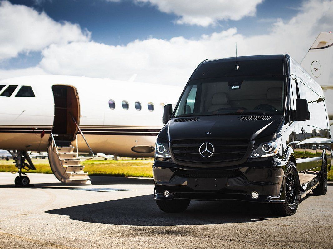 A happy family of four is taking a selfie at Chicago O'hare airport terminal 1. They have just been provided airport transportation by Rockford Rides Limo Service. The father, holding the smartphone, has a beaming smile and casual attire. Next to him is the mother, smiling warmly, standing close to their teenage daughter, who has a playful expression. Their young son is in front, looking up with a joyful grin. The background shows the bustling chicago airport ambiance with departure boards and passengers walking by. Luggage is visible at their feet, indicating travel plans.