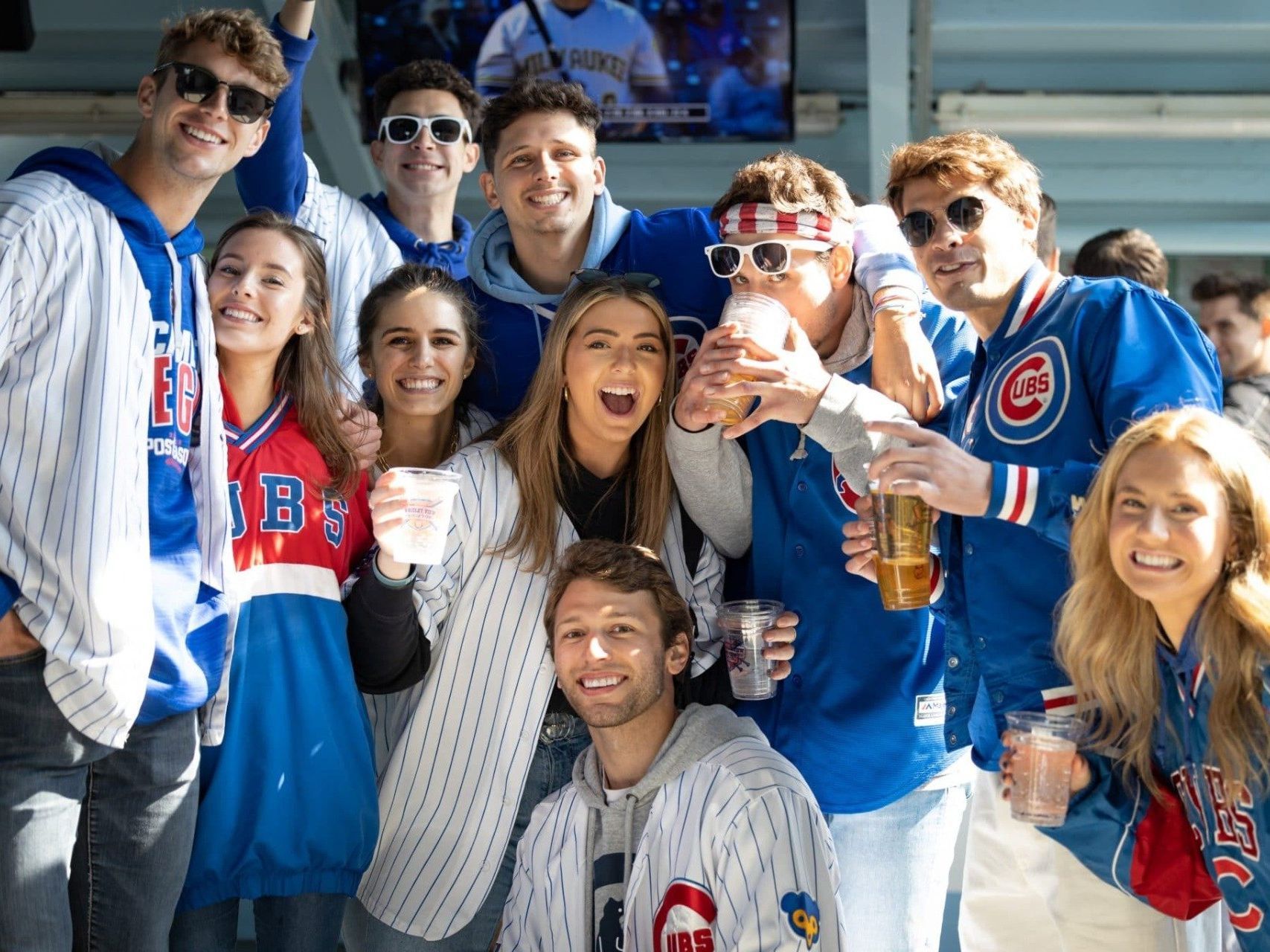  jubilant baseball fans, dressed in Chicago Cubs attire, are celebrating at a game.