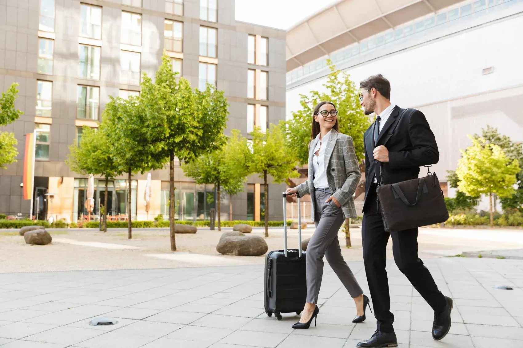 Two business professionals, a man and a woman, are briskly walking side by side with sunny outdoors.