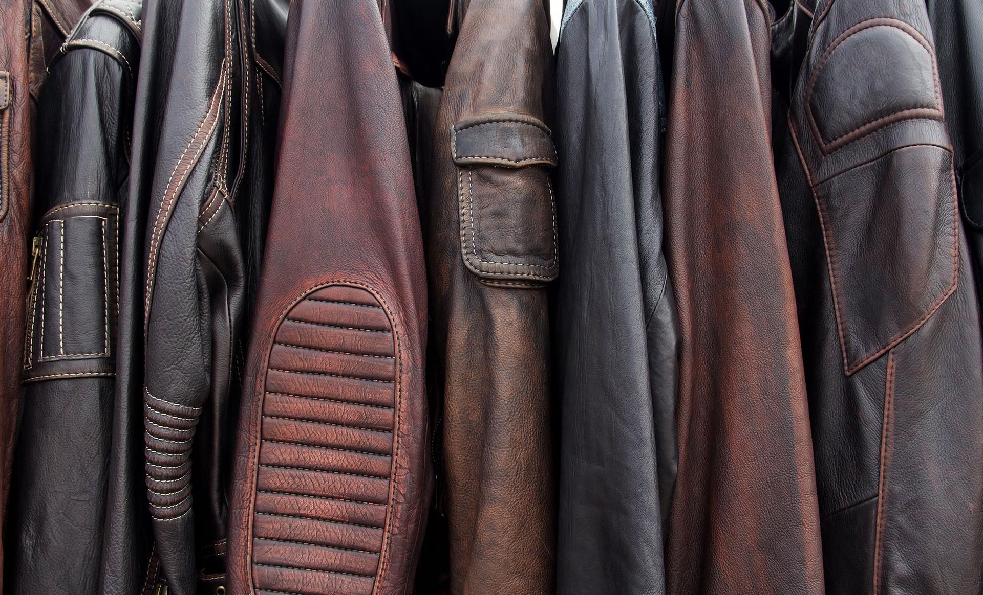 A bunch of leather jackets are hanging on a rack.