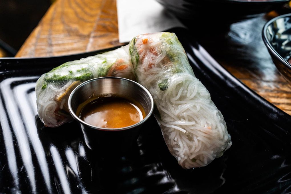 Two spring rolls with dipping sauce on a black plate.