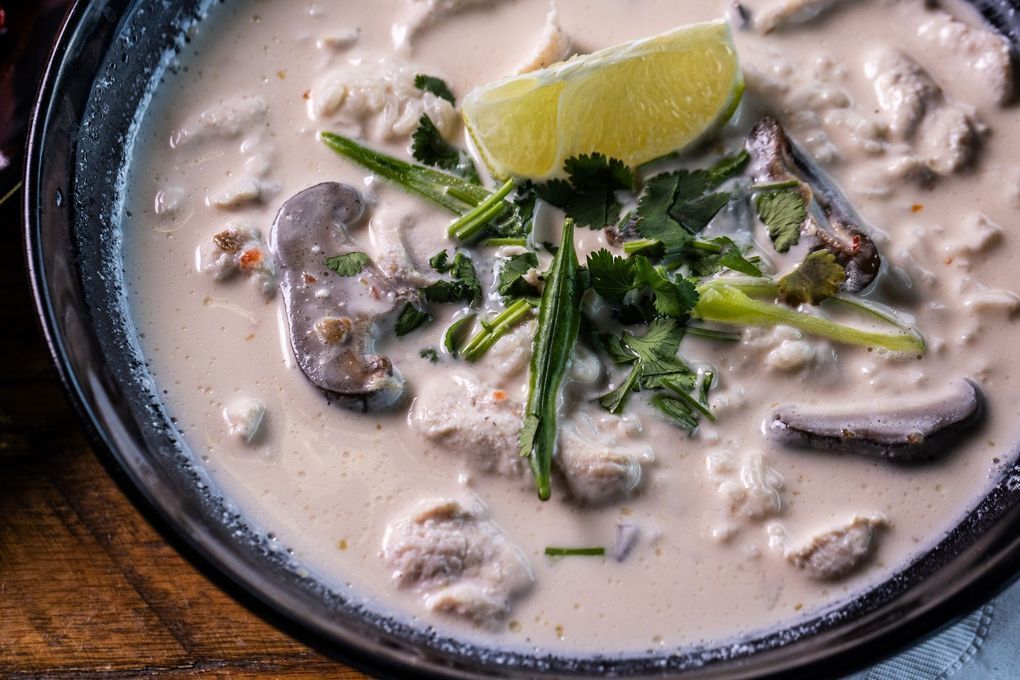 Creamy Thai soup with chicken, mushrooms, lime wedge, and cilantro in a dark bowl.