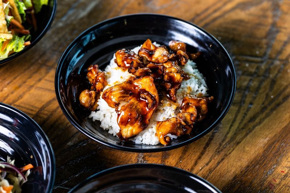 Chicken teriyaki over rice in a black bowl on a wooden table.