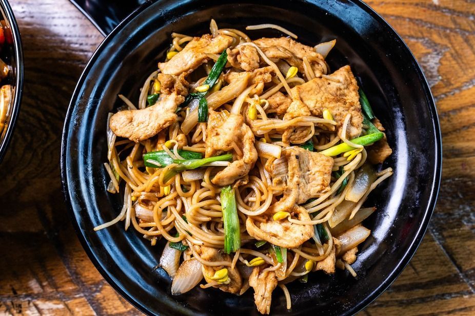 Chicken noodles with green onions and bean sprouts in a black bowl.