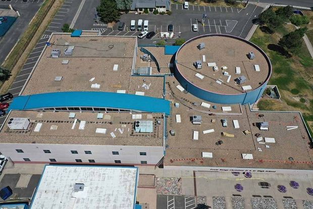 Aerial view of a building with a blue facade, flat roof, and surrounding parking lot and vegetation.