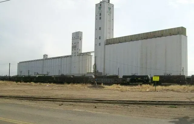 Large white grain elevator complex next to railroad tracks.