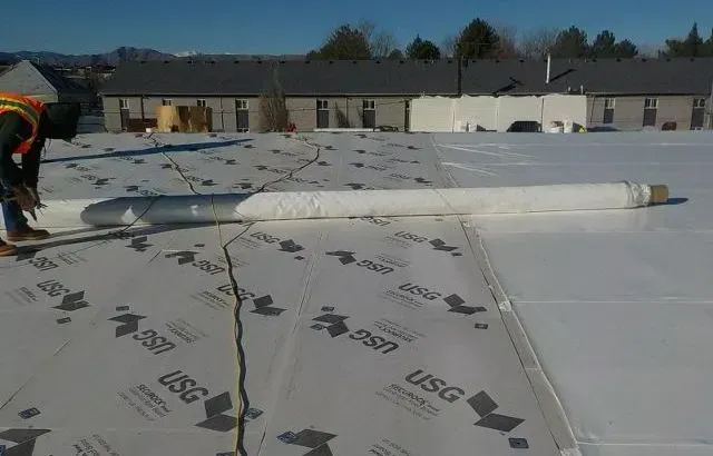 Roofer on a flat roof unrolling white roofing material next to a roll of membrane.