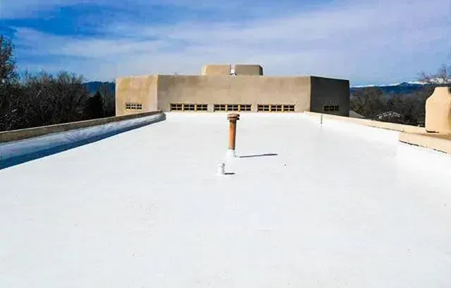 White flat roof with chimney vent and a building with windows, under a blue sky.