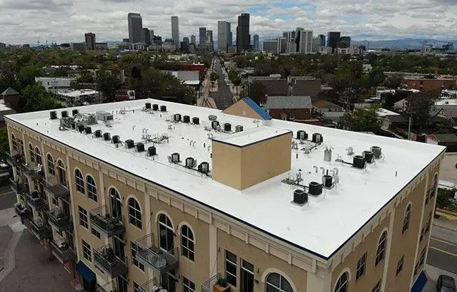 Building rooftop with numerous AC units, city skyline in the background.