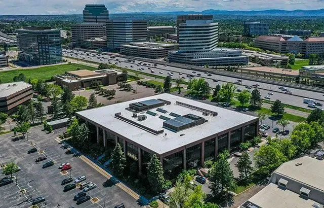 Aerial view of a square, low-rise building surrounded by a parking lot, trees, and other office buildings in a city.
