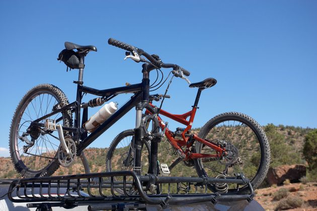 Two mountain bikes mounted on a car rack under a blue sky.