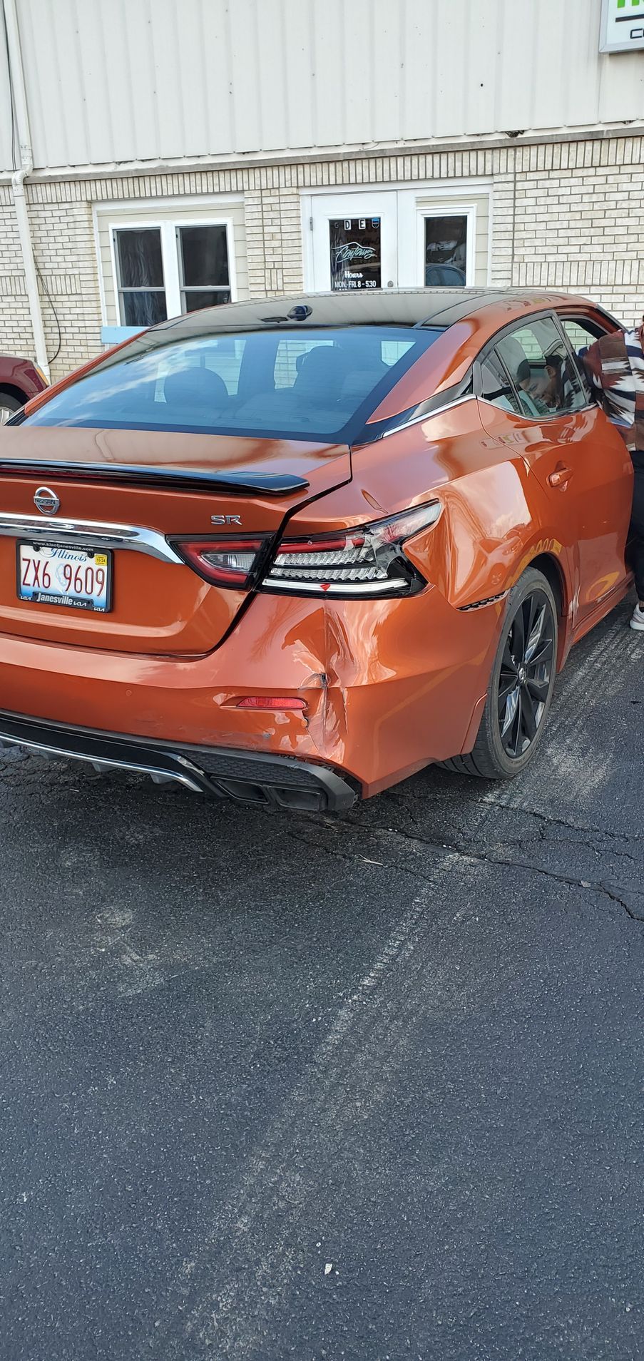 A damaged orange car is parked in a parking lot in front of a building.